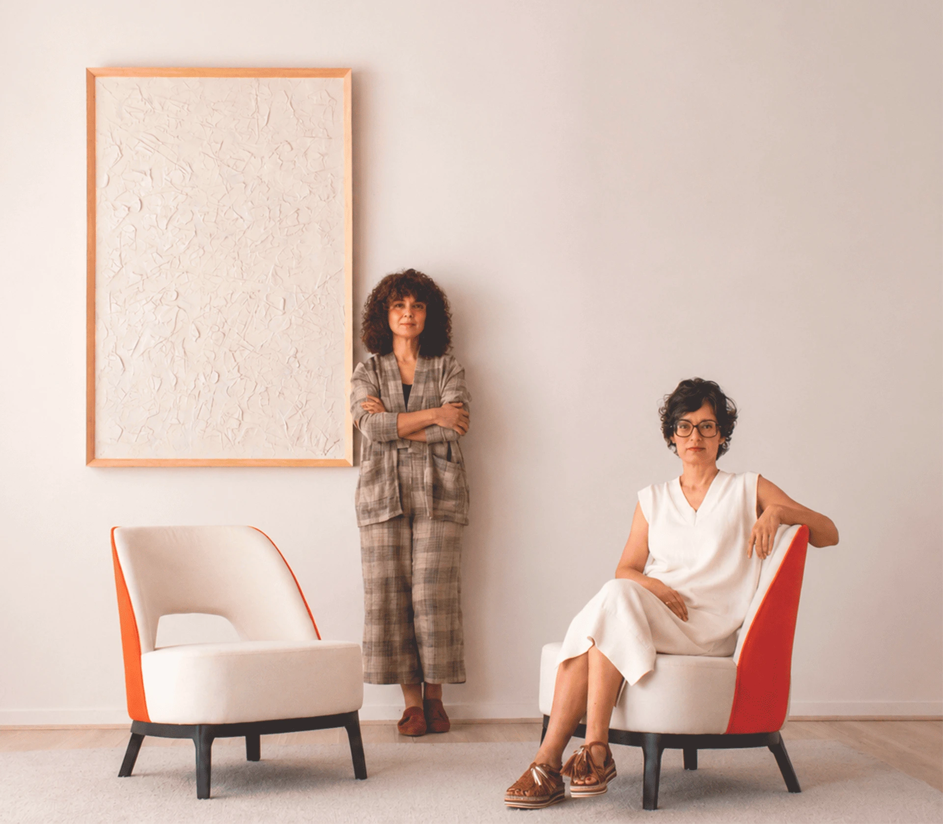 Verónica y Paula, gestoras de VP Interiorismo, en la sección sobre la empresa junto a dos butacas de diseño contemporáneo y cuadro con textura de la colección.