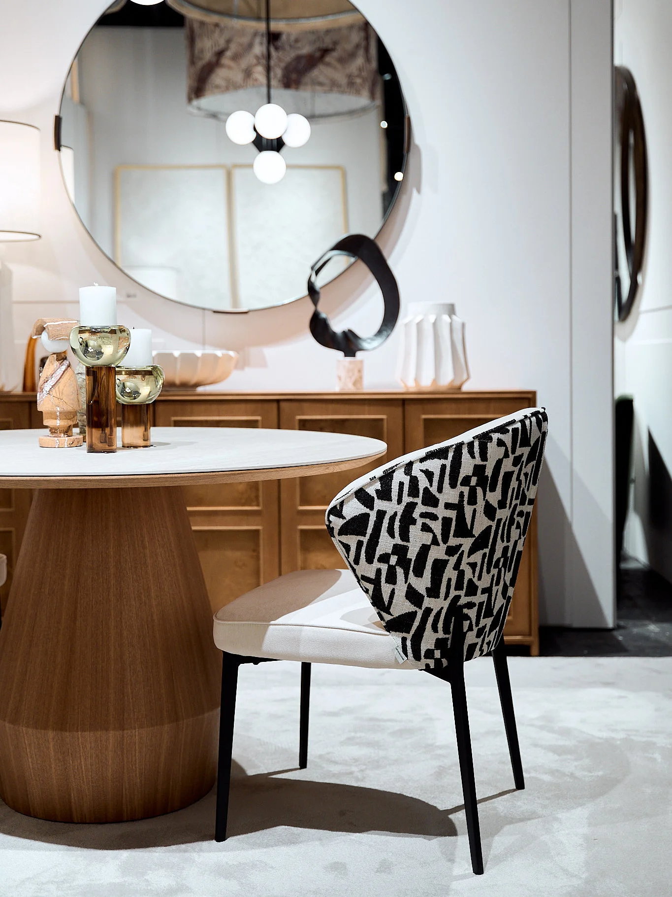 Mesa de comedor redonda en madera noble con silla tapizada en estampado abstracto blanco y negro.